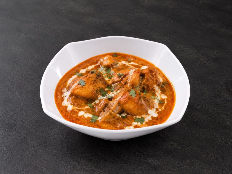 Creamy orange butter chicken curry in a white bowl, swirled with cream and scattered with coriander