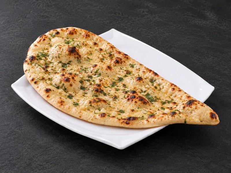 Garlic naan brushed with butter and scattered with chopped coriander on a white plate