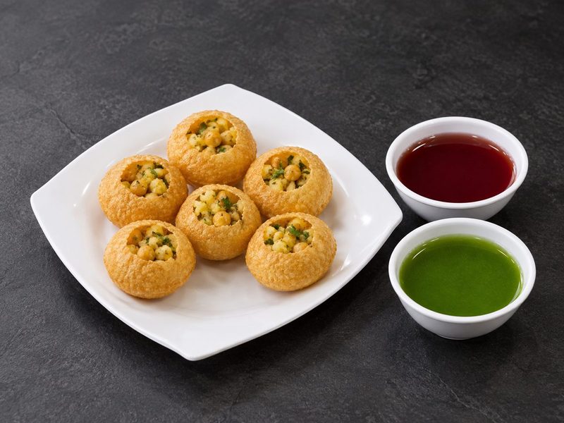 Six crisp pani puri shells filled with chickpeas and potato, served with bowls of red and green water