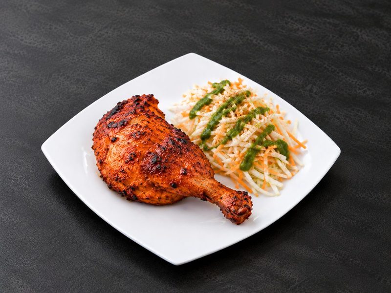 Charred red tandoori chicken leg quarter with shredded carrot and cabbage salad drizzled with green chutney